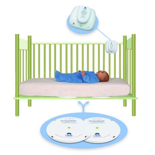Baby lying in a green crib with monitoring devices above and below, illustrating a baby monitoring system.