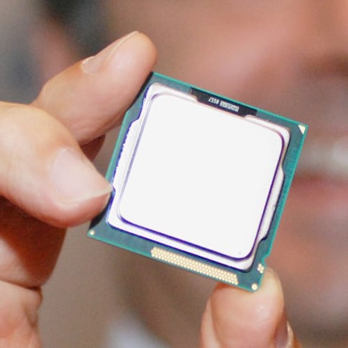A person holding a computer processor chip between their fingers. The chip features a metallic, reflective surface and is situated against a blurred background.