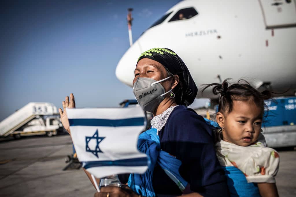 13 October 2021, Israel, Tel Aviv: New Jewish emigrants from the Bnei Menashe (sons of Manasseh) community in India, hold Israeli flags as they cheer upon arrival at Ben Gurion Airport near Tel-aviv. 250 emigrants of Bnei Menashe community, claimed to be one of the Ten Lost Tribes of Israel that settled in India, have arrived today in Israel as part of an operation by the Ministry of Aliyah and Integration (Immigrant Absorption). Photo: Ilia Yefimovich/dpa (Photo by Ilia Yefimovich/picture alliance via Getty Images)