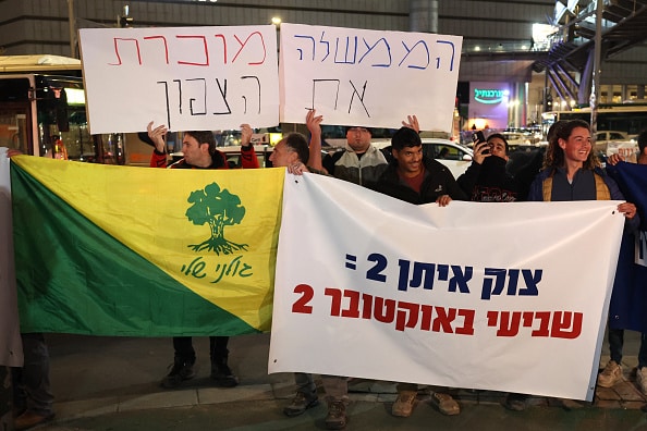 Demonstrators raise placards and Israeli flags during a protest in front of the Israeli Defence Ministry in the coastal city Tel Aviv on November 26, 2024, against a possible ceasefire with Hezbollah in Lebanon. Israel's security cabinet has started discussing a proposed ceasefire deal in its war with Hezbollah in Lebanon, an Israeli official confirmed to AFP on November 26. (Photo by Jack GUEZ / AFP) (Photo by JACK GUEZ/AFP via Getty Images)