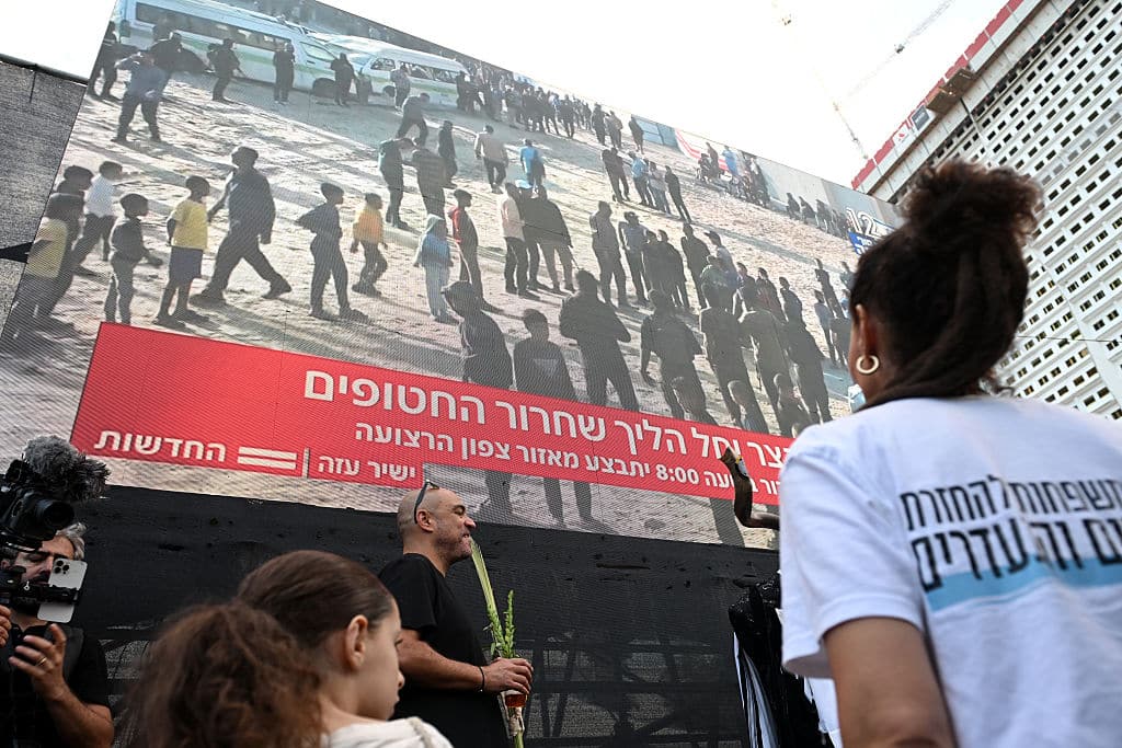 TEL AVIV, ISRAEL - OCTOBER 13: People watch a large screen broadcasting a live feed of Gaza, as they wait for the start of the hostage release at Hostages Square on October 13, 2025 in Tel Aviv, Israel. The ceasefire deal between Israel and Hamas has brought an end to the two years of war that followed the attacks of Oct. 7, 2023. A condition of the deal was the immediate return of 48 hostages held in Gaza, around 20 of whom were believed to be alive. (Photo by Alexi J. Rosenfeld/Getty Images)
