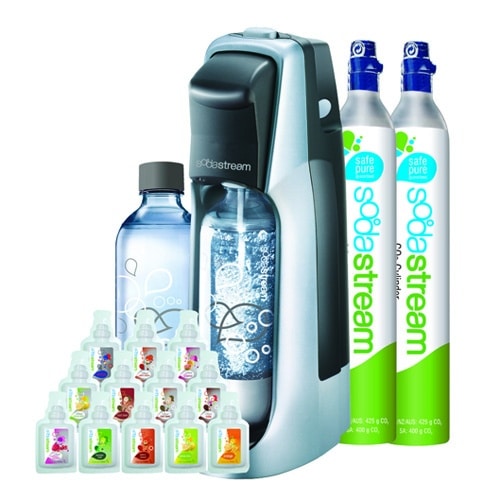 Soda machine with a clear carbonating bottle, two CO2 canisters, and various flavor syrup bottles arranged in front. The canisters and soda machine both read SodaStream with graphic designs of bubbles on them.